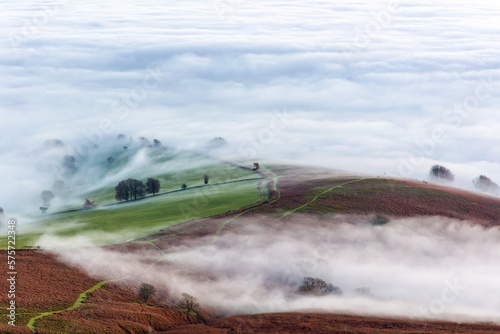 Farmland and rolling hills rising above a thick layer of fog in a rural area (Brecon Beacons)