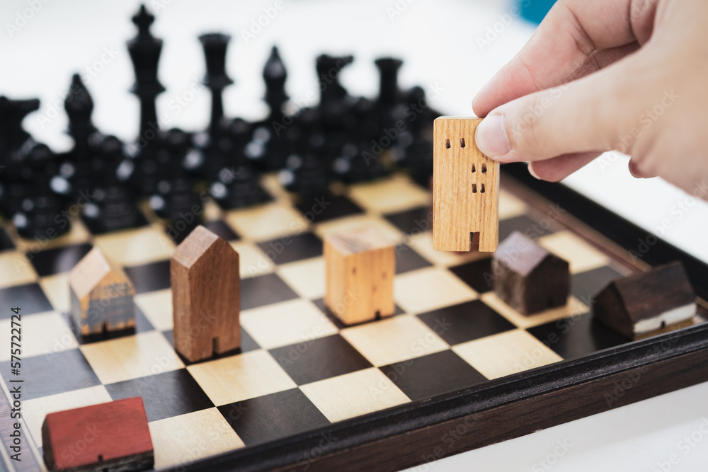 Hand of business man moving chess to Building and house models in chess game, competition success play. strategy, management or leadership concept Hand of business man moving chess to Building and house models in chess game, competition success play. strategy, management or leadership concept