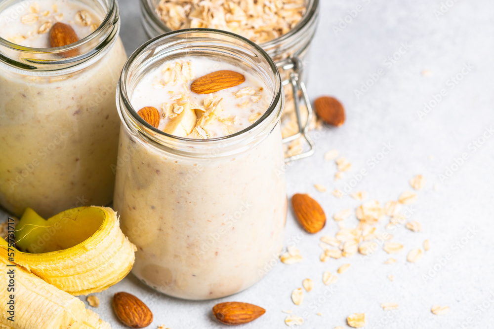 Almond banana smoothie with oat flakes in glass jars at white table. Almond banana smoothie with oat flakes in glass jars at white table.