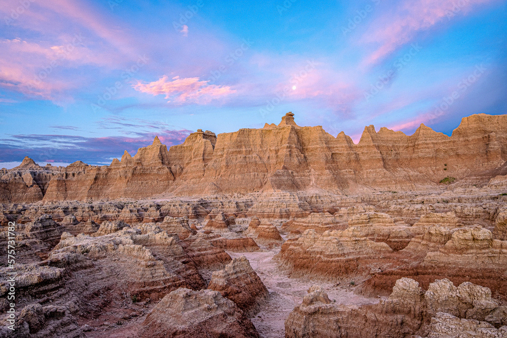 Fototapeta premium Pink sunrise clouds and full moon over rock formations in Badlands National Park