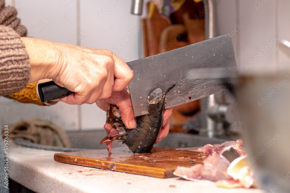 A woman cuts fish with a large knife at home in the kitchen A woman cuts fish with a large knife at home in the kitchen