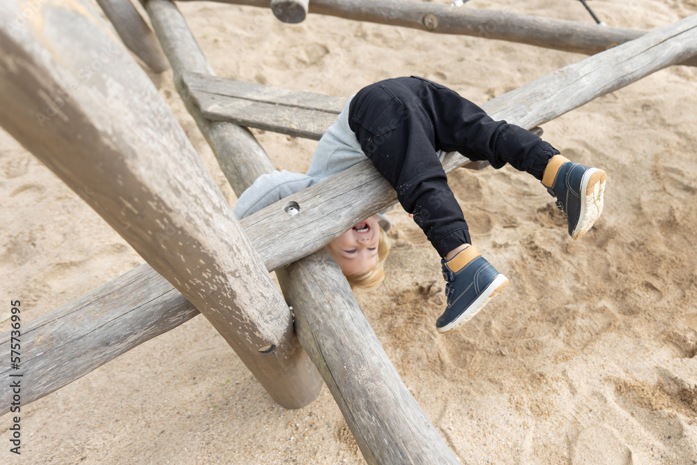 A little boy playing on a children's playground - flips himself over wooden log A little boy playing on a children's playground - flips himself over wooden log