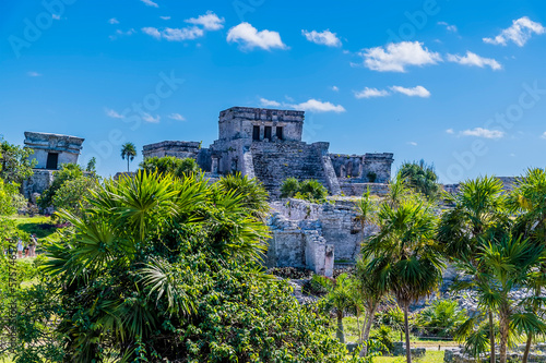 A view past trees towards temple ruins at the Mayan settlement of Tulum, Mexico on a sunny day