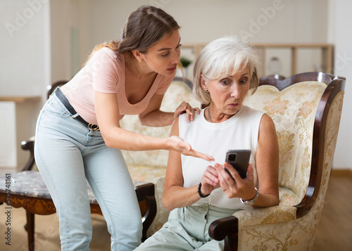 Senior mother and daughter using smartphone together at home