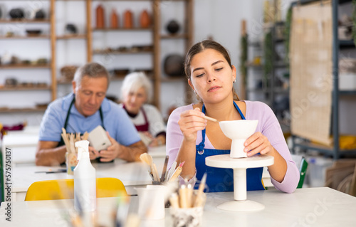 Woman using a spatula and a knife creates dishes from soft clay