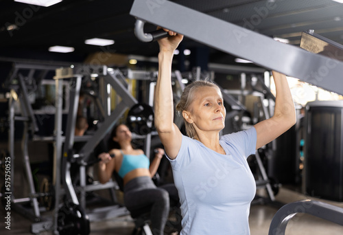 Older sportswoman training at shoulder press machine in gym