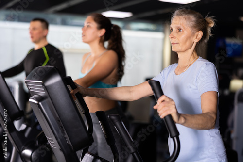 Older sportswoman training at elliptical machine in gym