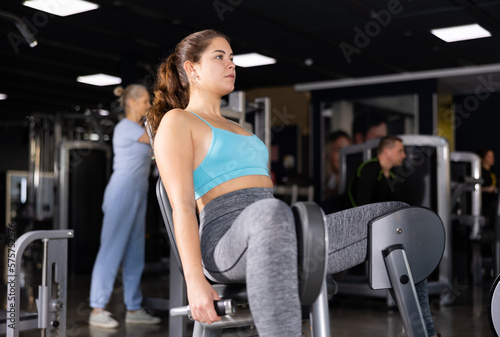Active young woman training at leg abductor machine in gym