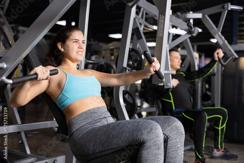 Young female training trains the muscles of the arms and press on the simulator in gym. Sport concept
