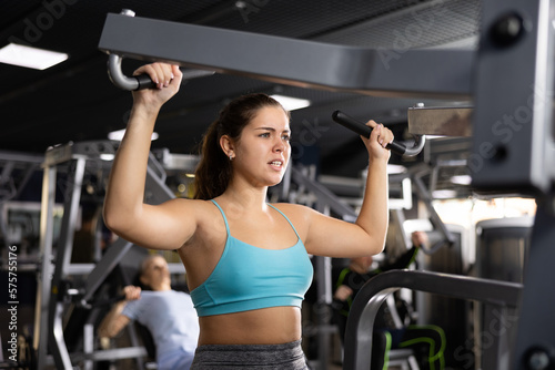 Fit young woman working out at shoulder press machine in gym