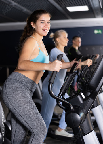 Sporty young woman using elliptical machine in gym