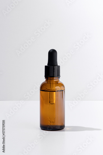Natural essential oil or serum for women's skin care on a white isolated background. Mockup of container with dropper lid with collagen in rays of hard sunlight.