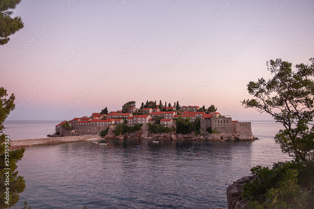 Panoramic view of Sveti Stefan in Montenegro at pink sunset. Famous tourist place near Budva. Natural beautiful island, with terracotta roofs among the turquoise sea. Copy space, wallpaper background