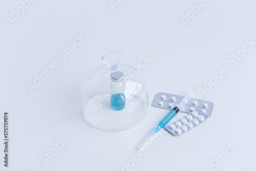 On white isolated background lie a syringe with medicine, a vial with a blue vaccine against viruses, pills for flu, colds. Medical preparations for the fight against the epidemic. Mock up, copy space