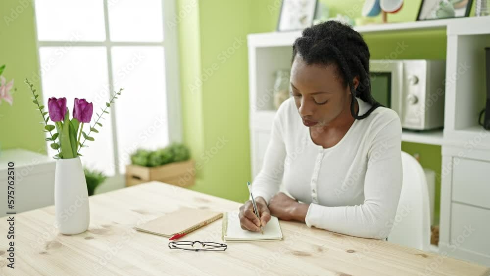 African american woman writing on notebook sitting on table at home African american woman writing on notebook sitting on table at home