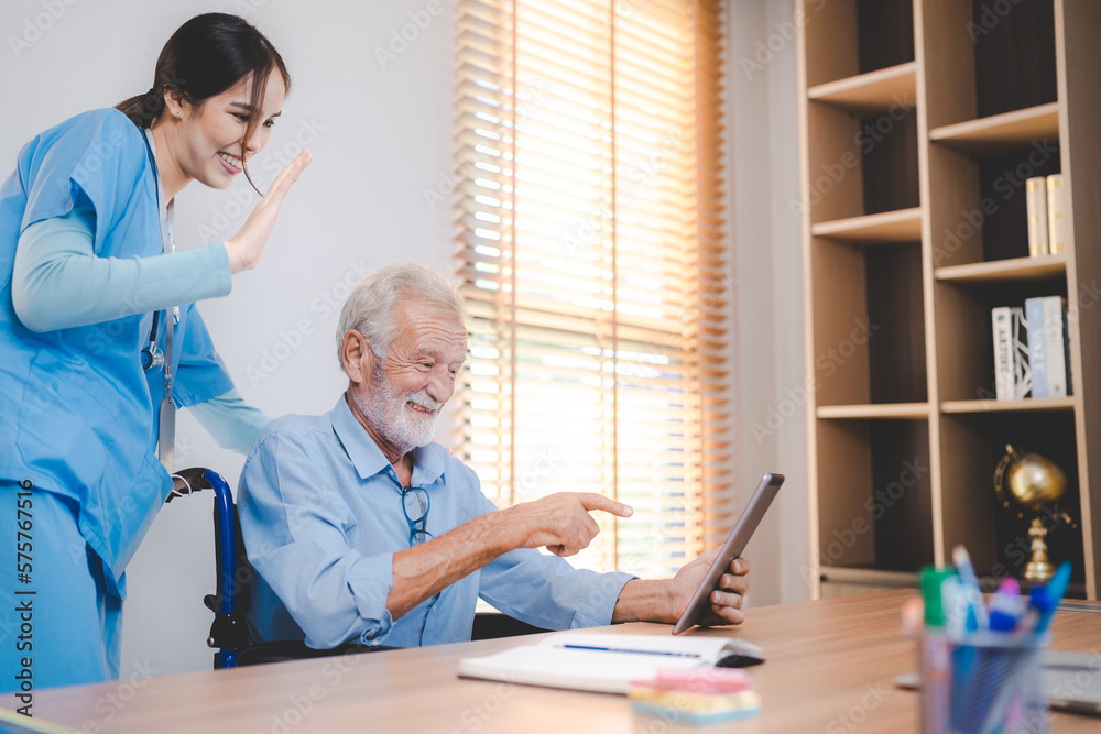 Fototapeta premium Smiling and cheerful senior male patient using digital tablet for video call with nurse in uniform and stethoscope standing waving hand at screen in a medical room in hospital