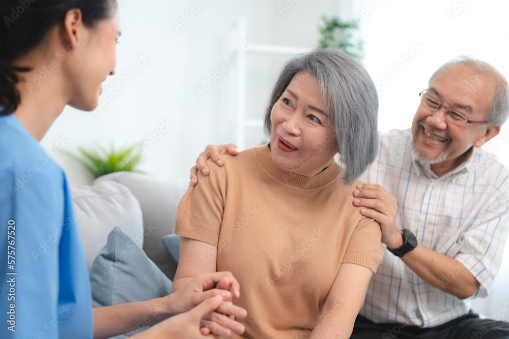 Obraz premium Smiling young nurse in uniform sitting with senior male and female couple at home assuring and building them in confidence about recovery in health