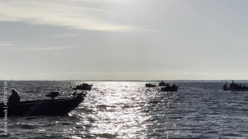 Silhouetted fishing boats glide across a glittering lake in morning Silhouetted fishing boats glide across a glittering lake in morning