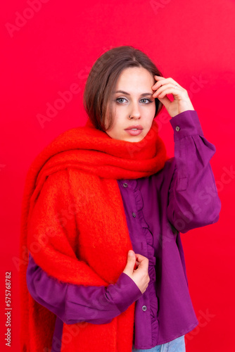 Close up portrait of a young caucasian woman in purple shirt isolated on red background, wearing a scarf looking at camera
