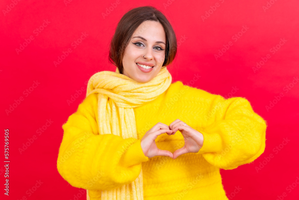 Young brunette woman wearing yellow sweater over isolated red background smiling in love making heart symbol shape with hands. romantic concept Young brunette woman wearing yellow sweater over isolated red background smiling in love making heart symbol shape with hands. romantic concept