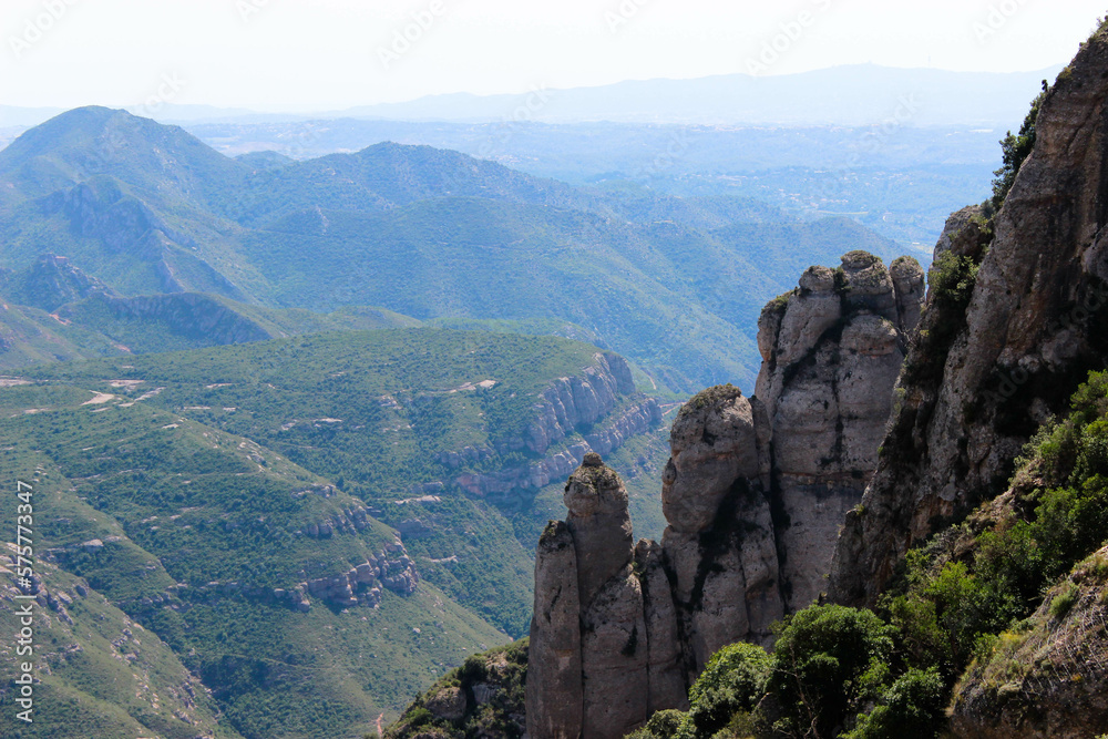 In the foreground is a mountain slope with finger-like rock formations and in the background a chain of smaller mountains.