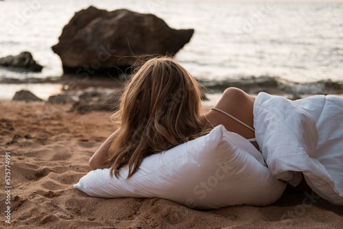 a girl in a white blanket walks along the beach at the sea, near the rocks. Beautiful, slender legs walk along the beach. Cream for varicose veins. High quality photo