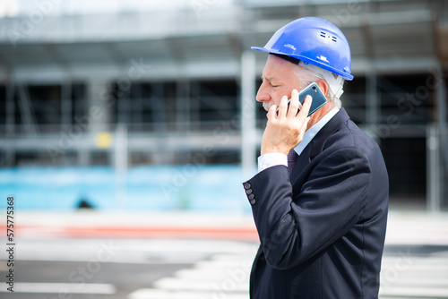 Architect talking on the phone outdoors in front of a construction site
