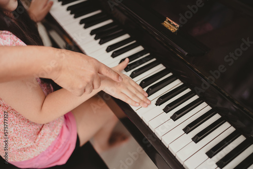 Cute and focused young little Asian girl practicing songs and melody with father and tutor while pressing white and black key and creating new music on piano as hobby and dedication at home