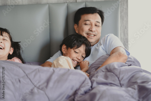 Handsome young Asian father embracing and hugging cute little Asian boy and son while preparing for for a good night sleep at home on a comfortable bed