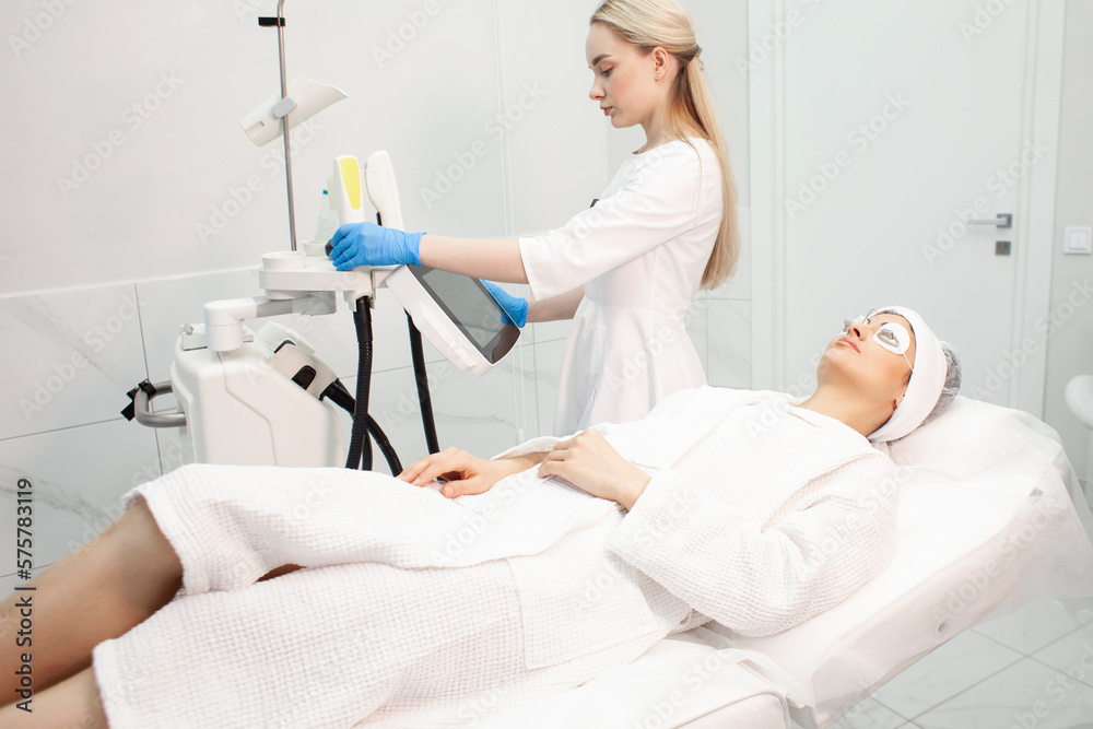 woman patient lies on couch in cosmetology clinic in protective glasses and smiles, girl at laser session