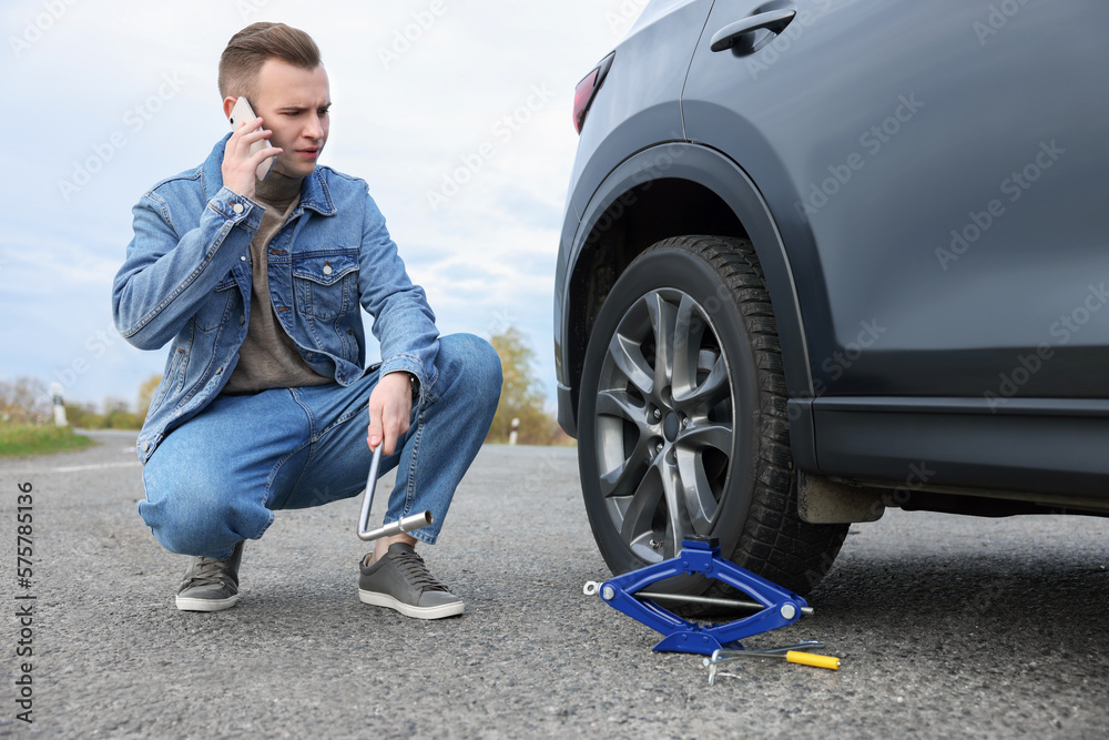 Worried young man calling car service. Tire puncture Worried young man calling car service. Tire puncture