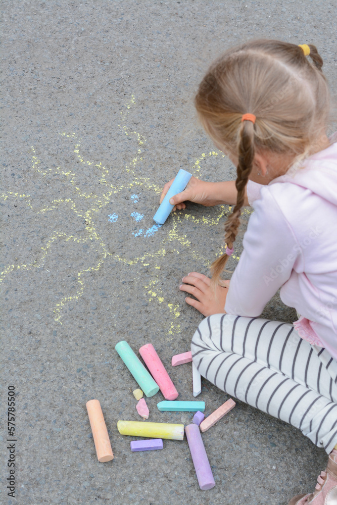 Naklejka premium Little child drawing sun with chalk on asphalt