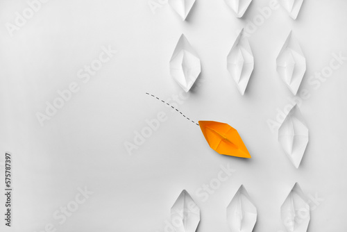 Yellow paper boat floating to others on white background, flat lay with space for text. Uniqueness concept