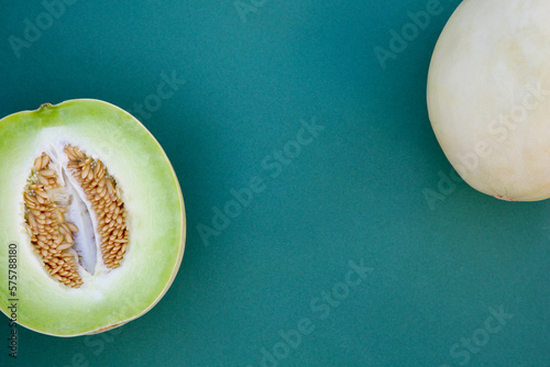 Whole and cut fresh ripe honeydew melons on teal background, flat lay. Space for text