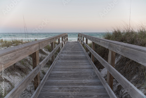 Straight wooden pathway with railings in between sand dunes against the ocean and horizon sky. Wooden walkway near the protected sand dune with grasses with views of ocean waves in Destin, Florida. © Jason