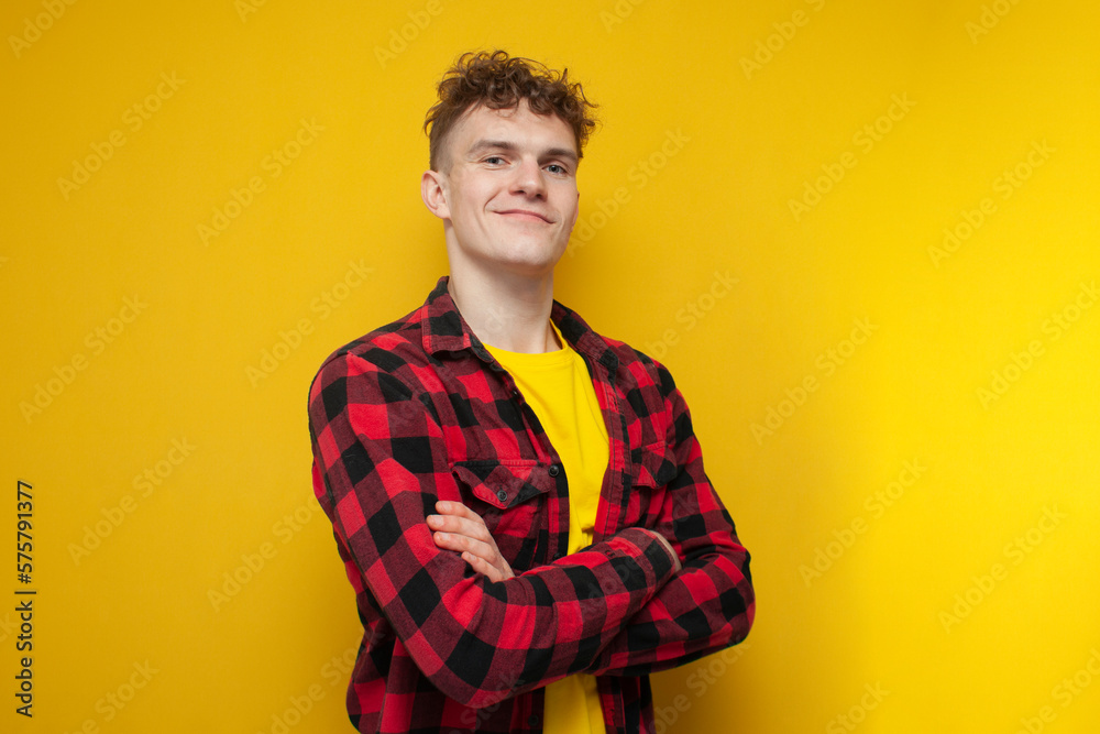 young confident guy in glasses with curly hair puts on a shirt on a yellow background young confident guy in glasses with curly hair puts on a shirt on a yellow background