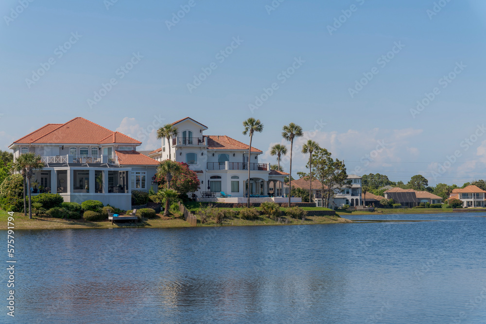 Rich neighborhood with mansions near Four Prong Lake in Destin, Florida. Mansions villas at the shore of the lake with plants and trees on its yards against the blue sky background.