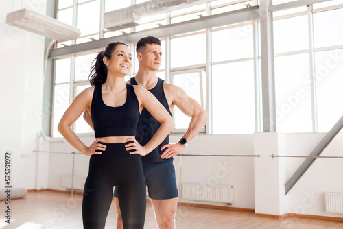 beautiful athletic couple in sportswear stands in the gym in the morning, fitness girl and coach man look to the side © Богдан Маліцький