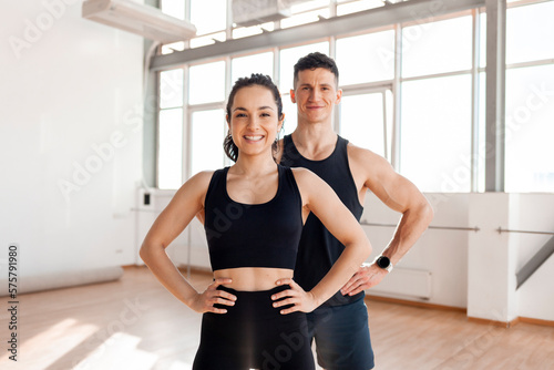 athletic couple in sportswear stands in the gym in the morning, fitness girl and coach man in training in bright room
