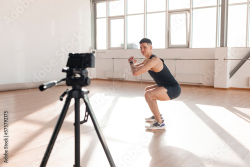 athletic guy records workout in the gym, male sports blogger squats and trains online