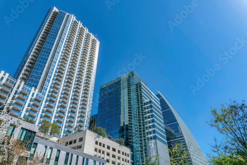 View of modern residential buildings at Austin, Texas. There are lower buildings at the front with a view of trees on the roof deck near the high rise buildings with balconies and glass exterior. © Jason