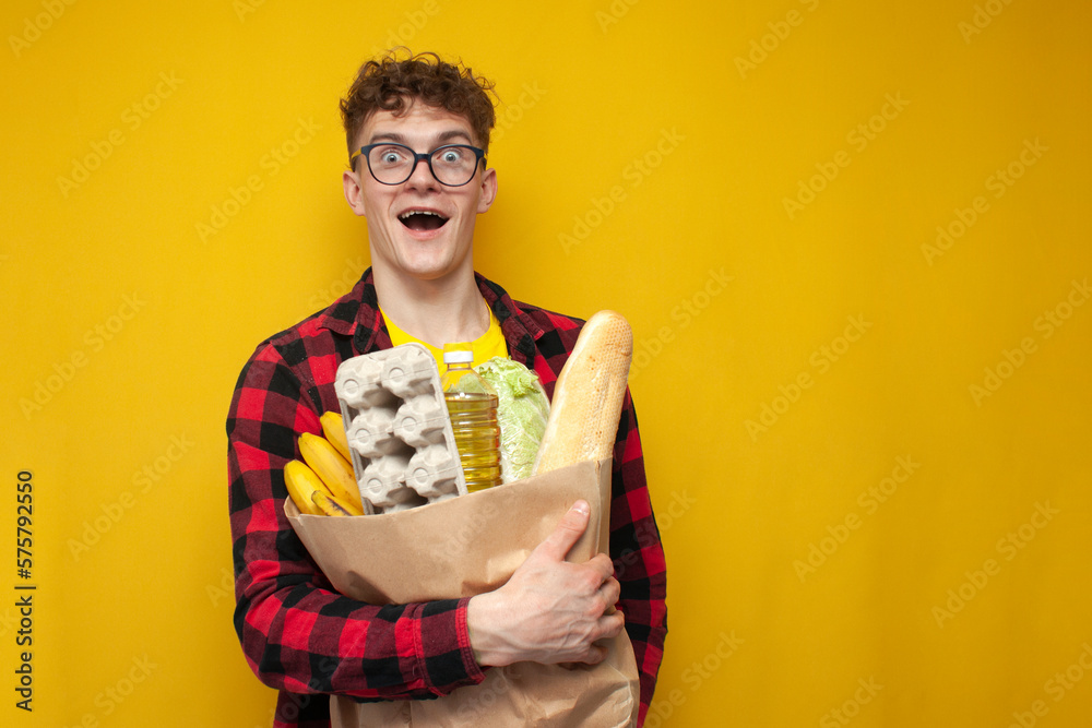 young shocked guy holds a package of groceries and is surprised on a yellow background young shocked guy holds a package of groceries and is surprised on a yellow background
