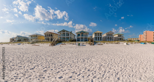 Beautiful and lavish beach homes overlooking white sandy shore in Destin Florida. Facade of waterfront multi-storey houses against blue sky and clouds background.
