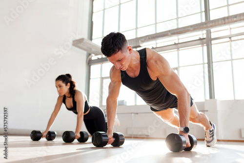 athletic couple in sportswear in training do push-ups with dumbbells in the fitness room in the morning