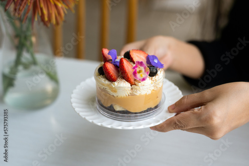 A Banoffee Pie is served in a plastic cup, adorned with flowers and strawberries as decoration.