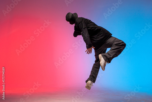 young guy falls upside down in the air, man levitates and flies down in neon lighting, acrobat dancer flies in jump