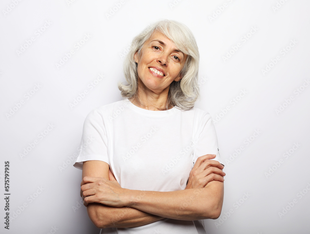 Smiling elderly woman wearing white t-shirt posing with crossed arms, over white background Smiling elderly woman wearing white t-shirt posing with crossed arms, over white background