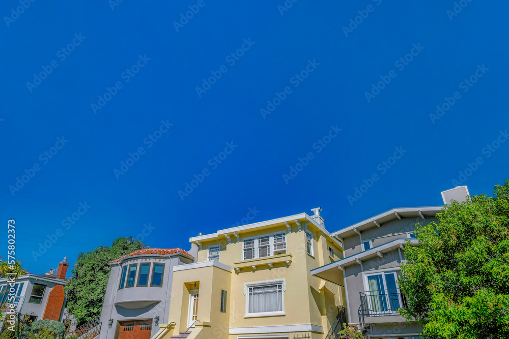 Homes with sunlit walls against blue sky viewed from the street in San Francisco. Facade of houses with balconies, outdoor stairs and bay windows. Homes with sunlit walls against blue sky viewed from the street in San Francisco. Facade of houses with balconies, outdoor stairs and bay windows.