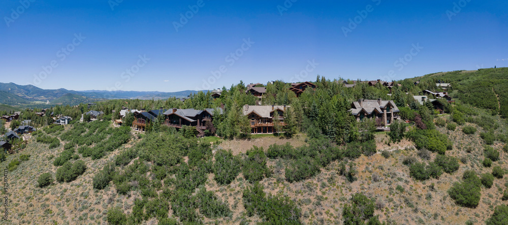 Aerial view of evergreen trees and houses in the mountains of Park City Utah. Panorama of a peaceful nature landscape with homes surrounded by lush foliage against blue sky.