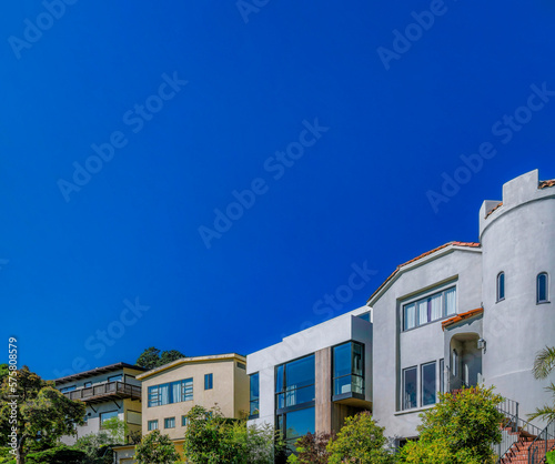 San Francisco California homes exterior view with beautiful architecture. Facade of multi-storey houses with lush trees and clear blue sky scenery on a sunny day. © Jason